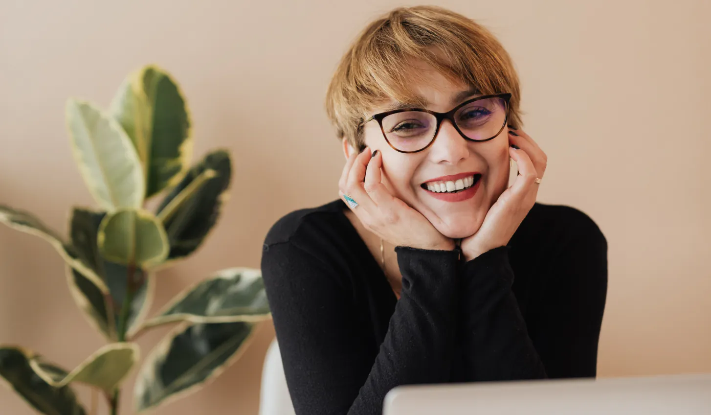 une femme à lunettes souriant en regardant un ordinateur portable