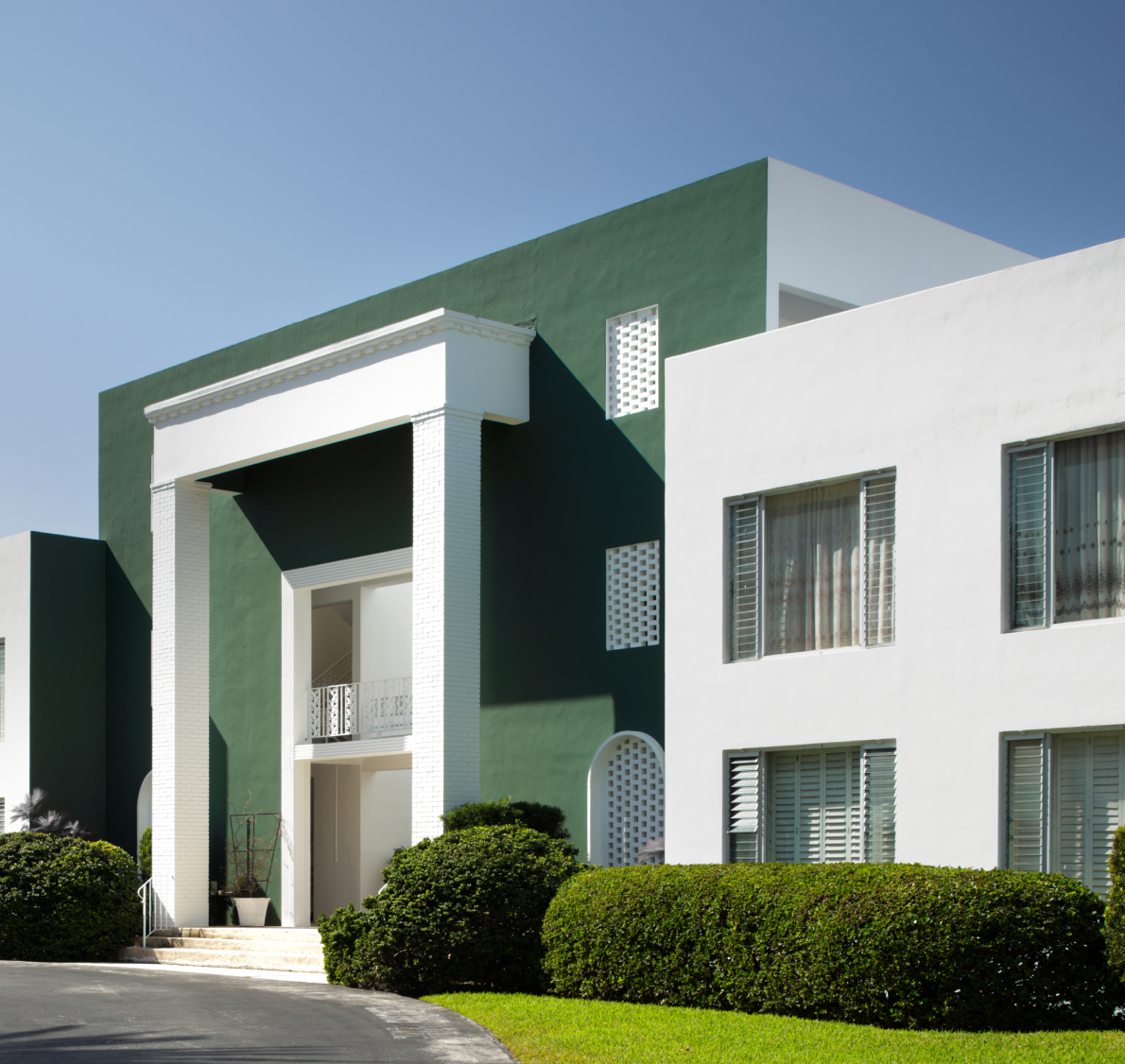 un bâtiment vert et blanc avec des buissons et des arbres