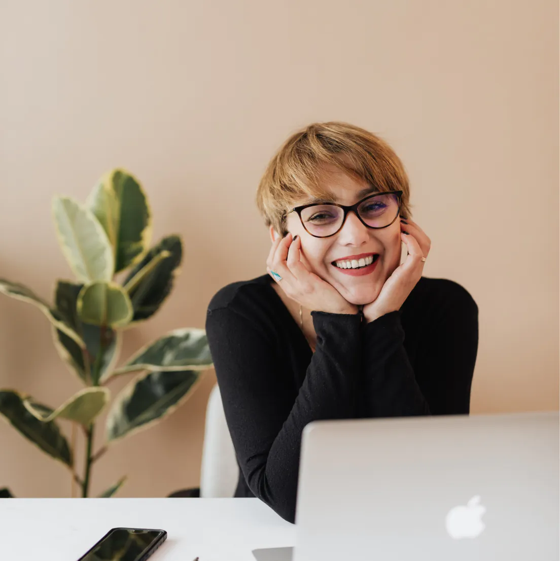 une femme à lunettes souriant en regardant un ordinateur portable