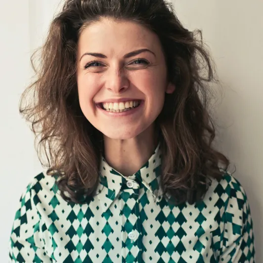 une femme aux cheveux longs souriant et portant une chemise verte et blanche 